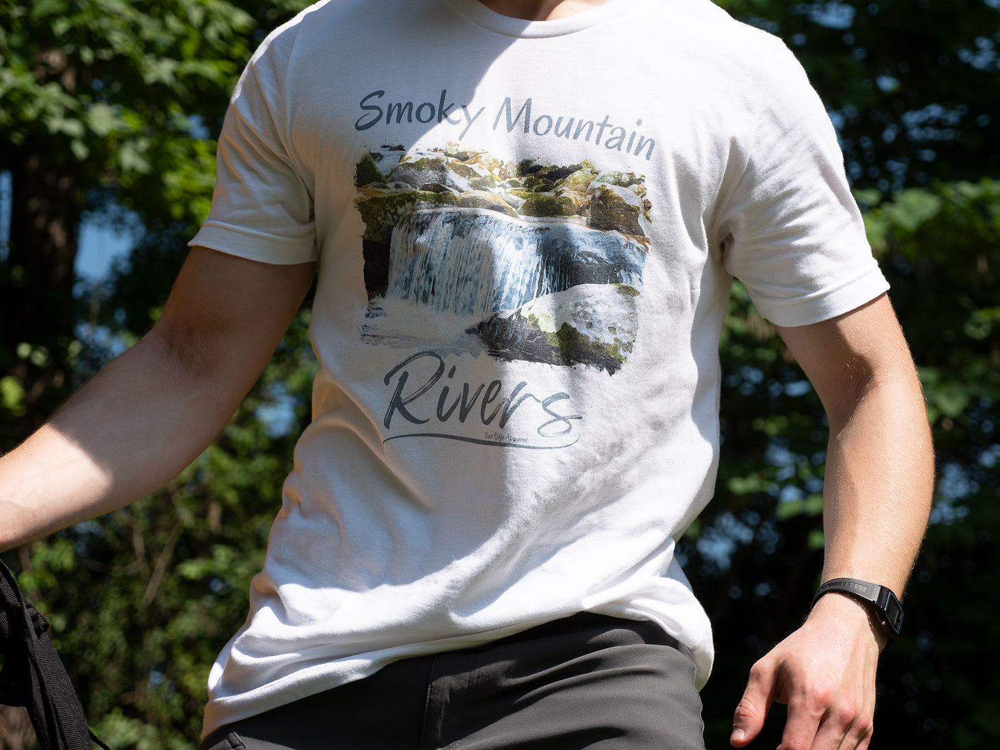 Smoky Mountain Rivers T-Shirt inspired by the Great Smoky Mountain National Park by East Ridge Apparel. Picture shows a person picking up a backpack with the Smoky Mountain Rivers T-Shirt by East Ridge Apparel in view.