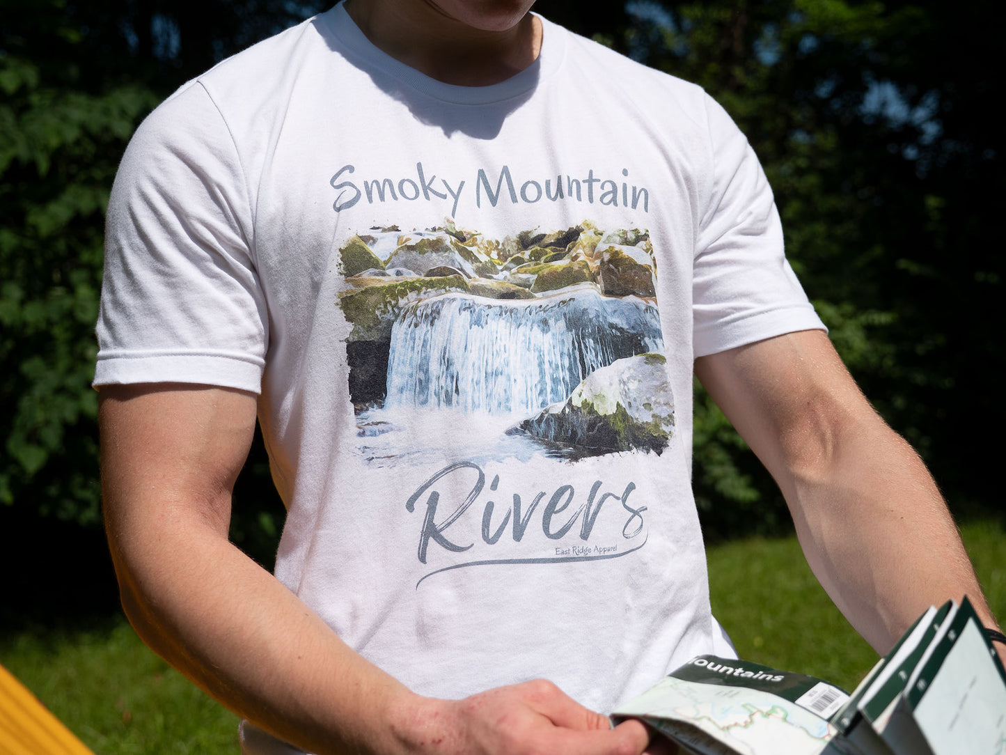 Smoky Mountain Rivers T-Shirt inspired by the Great Smoky Mountain National Park by East Ridge Apparel. Picture shows a person holding a Great Smoky Mountains National Park map with the Smoky Mountain Rivers T-Shirt in view.