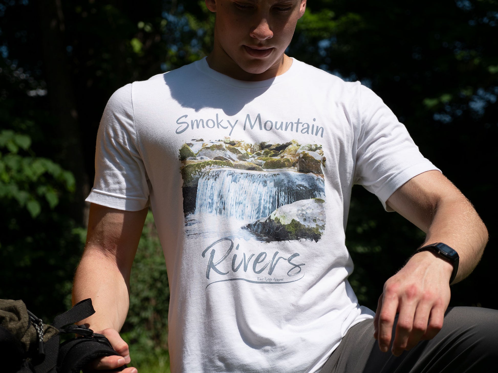 Smoky Mountain Rivers T-Shirt inspired by the Great Smoky Mountain National Park by East Ridge Apparel. Picture shows a person holding a backpack with the Smoky Mountain Rivers T-Shirt by East Ridge Apparel in view.